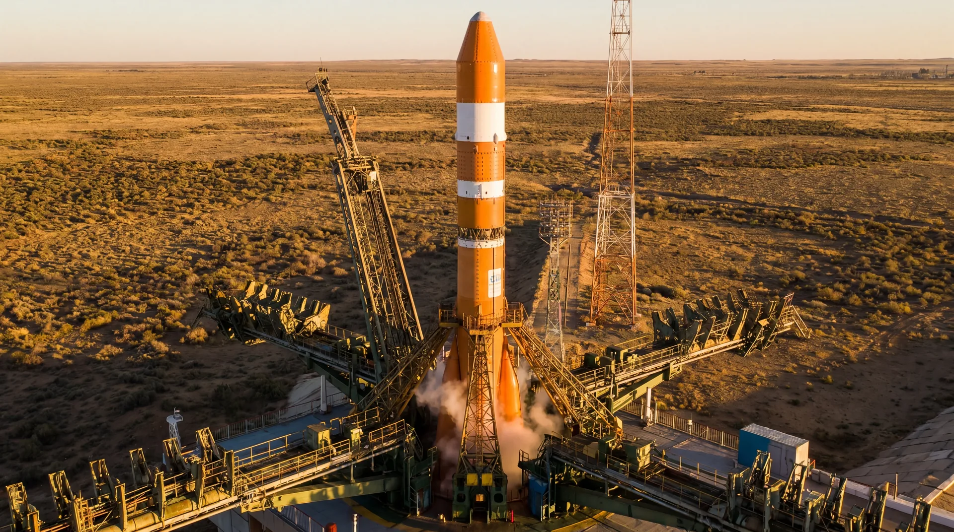 The tall, slender Soyuz-5 rocket standing on a launch pad under the warm light of a setting sun in the steppe.