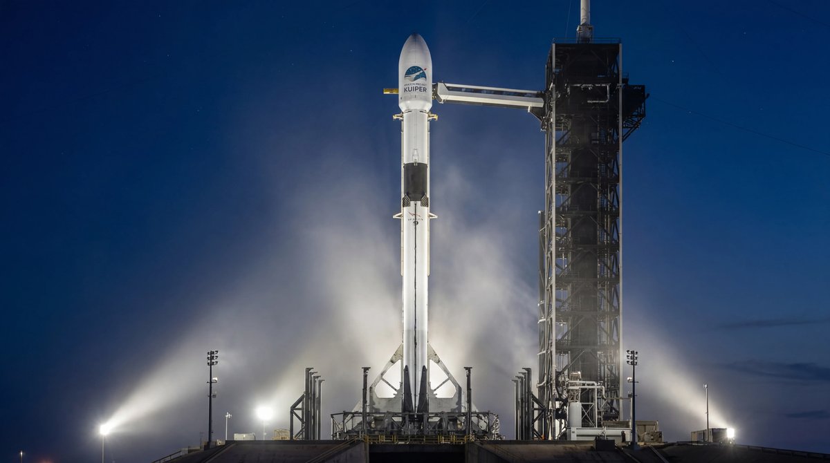 SpaceX Falcon 9 rocket vertical on a launchpad at twilight illuminated by bright floodlights against a deep blue sky