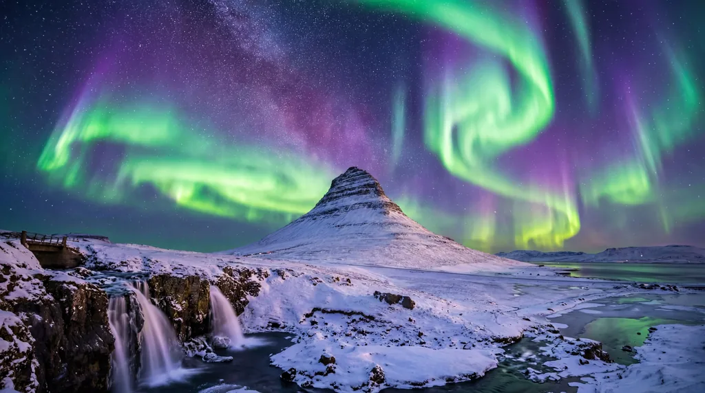 Intense green and purple northern lights swirling over the iconic Kirkjufell mountain in Iceland under a starry sky.