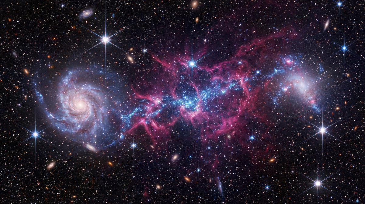 Two irregular galaxies connected by a glowing bridge of blue stars and pink gas against a deep starry space background.
