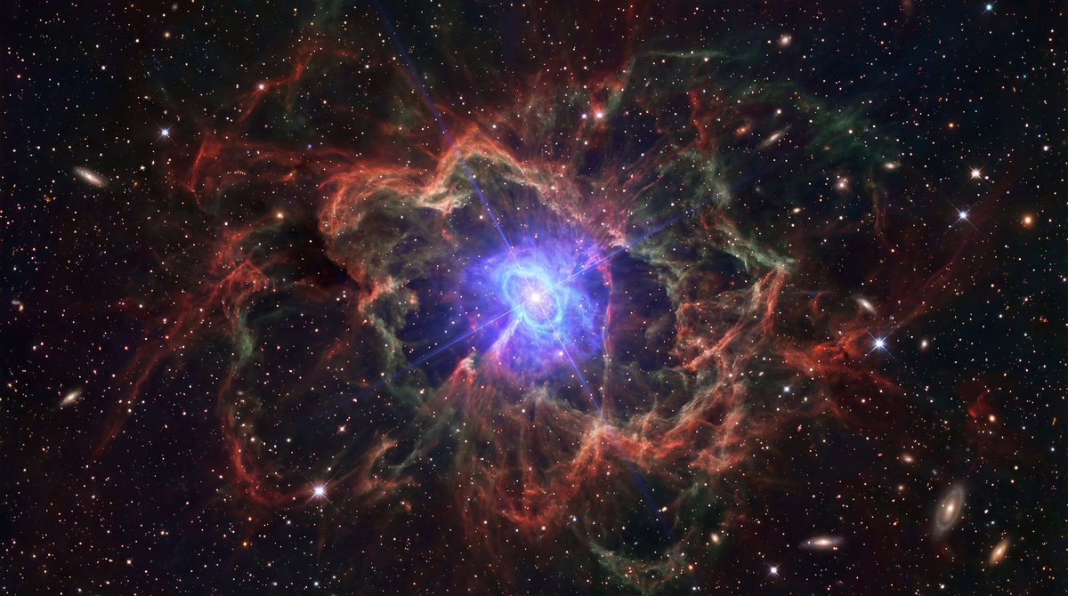 Swirling filaments of cosmic gas surround a bright blue central energy source against a field of distant stars.