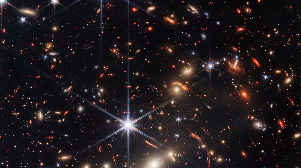 Thousands of colorful galaxies and red primitive stars fill a black deep space background, accented by bright spiked stars.