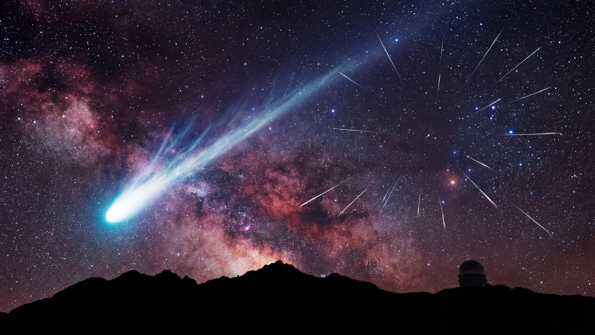 A comet and multiple meteor streaks illuminated against a dark, star-filled night sky above a silhouette landscape.